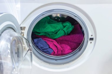 Çamaşır makinesinde duran renkli çamaşırların önünde açık bir kapı var..