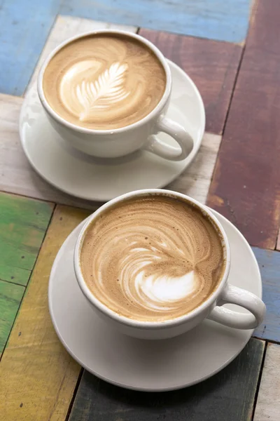 Dwie filiżanki kawy z latte art na drewnianym stole — Zdjęcie stockowe