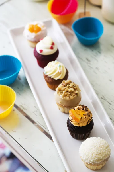 Colorful delicious cupcakes in row on plates — Stock Photo, Image