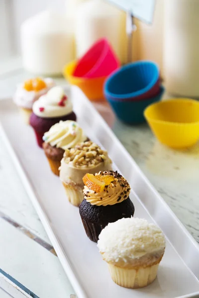 Colorful delicious cupcakes in row on plates — Stock Photo, Image