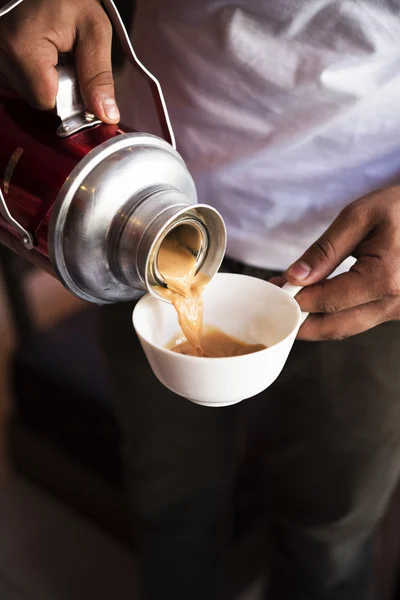 Hand pouring Traditional Indian masala tea into white ceramic cu — Stock Photo, Image