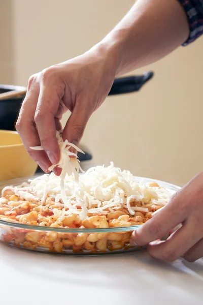 Hand adding cheese on top of macaroni — Stock Photo, Image