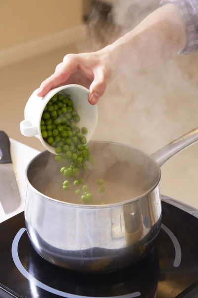 Hand adding pea into pot for making pea soup — Stock Photo, Image