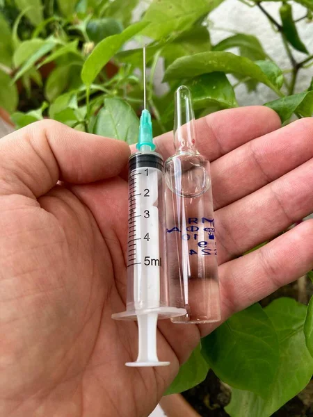 Kırmızı arka planlı bir şırınga ile bir şişe koronavirüs aşısı.