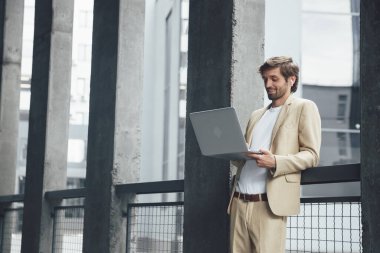 Yakışıklı iş adamı, ofis merkezinde dikilirken bilgisayardaki görüntülü konuşma için kablosuz kulaklık kullanıyor. İletişim ve teknoloji kavramı.