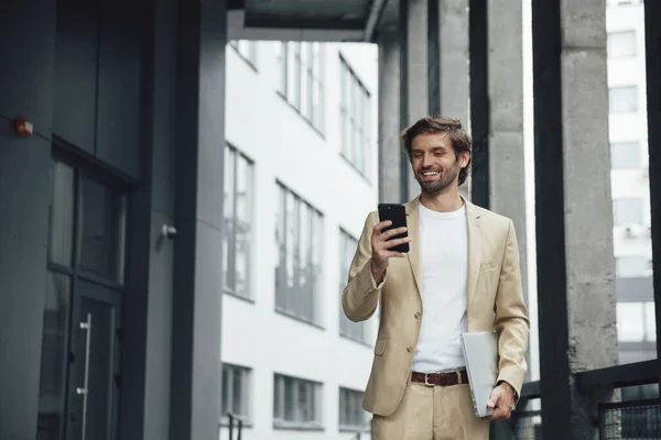 Resmi giyinmiş genç sakallı adam akıllı telefon ekranına bakarken mutluluğu hissediyor. Sokakta taşınabilir laptop taşıyan bir iş adamı. Dışarıdaki ofis binası..