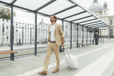 Kendine güvenen, şık takım elbiseli, beyaz bavullu, caddede yürüyen sakallı bir adam. Genç işadamı başka bir şehri ziyaret ediyor..
