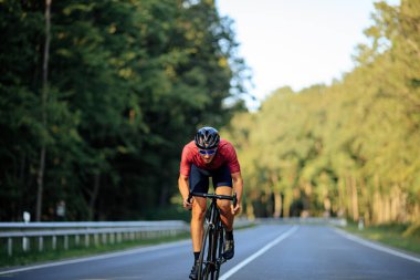 Koruyucu kasklı, gözlüklü ve spor kıyafetli yakışıklı adam kaldırım yolunda hızlı bisiklet sürüyor. Sabah sporu, temiz hava..