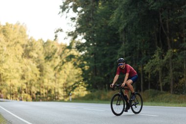 Güçlü bacakları olan yakışıklı bir adam sabah sporunu asfalt yolda yapıyor. Koruyucu kask takan, aynalı gözlük takan ve aktif kıyafet giyen bisikletçi. Motivasyon kavramı.