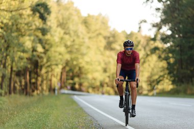 Açık havada bisiklet yarışında spor kıyafeti giymiş profesyonel yol bisikletçisinin ön görüntüsü. Miğferli genç adam temiz havada en sevdiği hobiyi yapıyor..