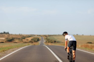 Asfalt yolda bisiklet süren, göz ve kask takan yakışıklı bir genç. Spor kıyafetleri eğitimi alan kaslı bir adam..