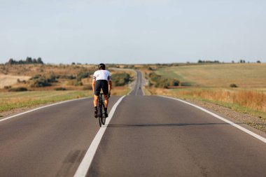 Spor kıyafetli, kasklı ve kırsal alanda bisiklet süren kasklı bir gencin arka görüntüsü. Spor aktivitesi ve düzenli eğitim kavramı.