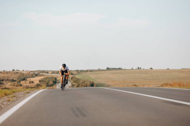 Spor elbiseli, koruyucu kasklı ve temiz havada bisiklet süren güçlü bir adam. Kaslı bisikletçi uzun mesafe yarışında pratik yapıyor..