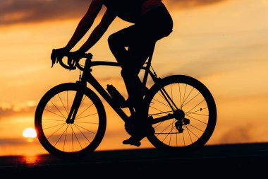 Arka planda güzel bir günbatımı olan asfalt yolda siluet bisikleti süren profesyonel bisikletçiye yakın çekim. Yarış kavramı.
