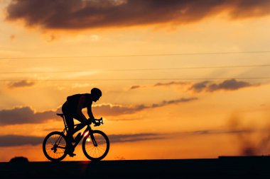 Siyahi motosikletle spor yapan profesyonel bisikletçinin yan görüntüsü. Yaz günbatımının arka planı. Bisiklet kavramı.