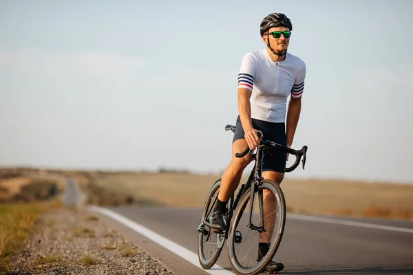 Spor kıyafetleri içinde güçlü genç bir atlet, siyah kask ve kırsal alanda bulanık bir geçmişi olan koruyucu gözlüklü bisiklet. Bisiklet ve eğitim kavramı.
