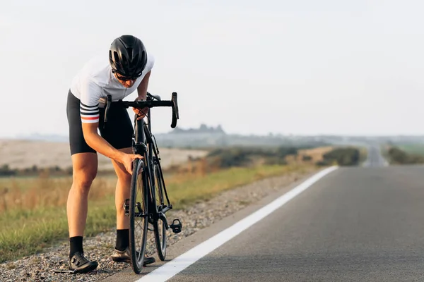 Bearded young man dressed in sport clothing checking the condition of bike wheel before riding on paved road. Concept of maintenance and sport.