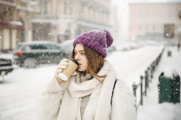 雪の中屋外に立ちながら 使い捨てカップから熱いフレッシュコーヒーを飲むかわいい若い女性 寒い冬の間に熱い飲み物で幸せな女性の温暖化 — ストック写真