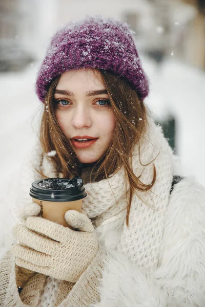 寒い冬の日の間に熱い飲み物を楽しんでニット帽 スカーフ 白いジャケットでかなり若いブルネット 幸せな女性が通りを歩いてコーヒーを手に — ストック写真