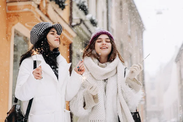 暖かい服を着た若い女性が目を閉じ 輝きを保持して通りに立って満足しました 2人の女性の友人は雪の日に屋外で余暇を過ごす — ストック写真