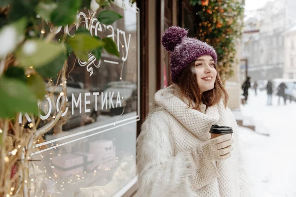 暖かい服を手に熱いコーヒーを保持する喜びの若い女性は カメラにポーズを取り 脇を見て 雪の冬の天気 — ストック写真