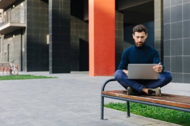 Dışarıda dizüstü bilgisayarda çalışan sakallı adam.