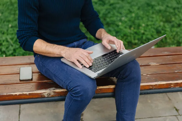 Freelancer masculino sentado en el banco y trabajando en el ordenador portátil — Foto de Stock