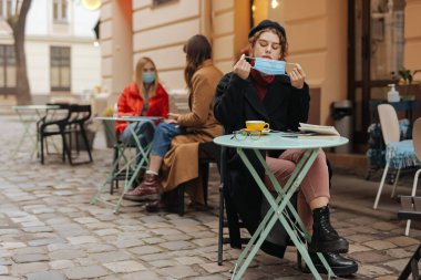 Yerel kafede sıcak kahve içtiği için maskesini çıkaran çekici genç bir kadın. Güzel bayan karantina sırasında masada tek başına oturuyor..