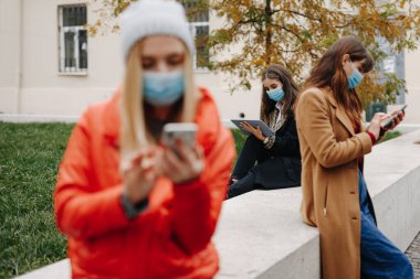 Tıbbi hijyen maskeli çekici kadınlar salgın sırasında açık havada mesafelerini koruyorlar. Gençler boş zamanlarını temiz havaya harcayıp modern aletler kullanıyorlar..