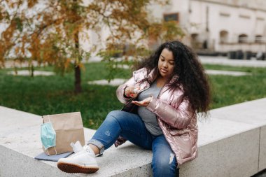 Güzel bir Afrikalı kadın temiz havada oturuyor ve elleri için antiseptik kullanıyor. İnsanlar, hijyen ve güvenlik kavramı.