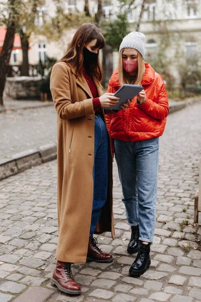 通りに立っている間暖かい服を着てデジタルタブレットを保持若い女性の完全な長さの肖像画 検疫中に医療保護マスクを身に着けて幸せな女性 — ストック写真