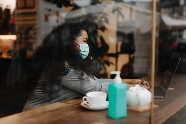 Kafede Oturmuş Dizüstü Bilgisayarla Çalışan Tıbbi Maskeli Afrikalı Bir Kadın — Stok fotoğraf