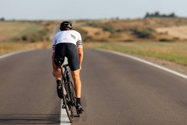 Siyah kasklı ve aktif giyimli erkek sporcunun güneşli bir günde dışarıda bisiklet sürüşü. Genç adam daha iyi formlar ve sonuçlar için düzenli olarak eğitim görüyor..