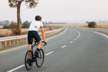Beyaz tişörtlü, siyah şortlu ve temiz havada bisiklet süren aktif bir adam. Rekabet ve düzenli eğitim kavramı.