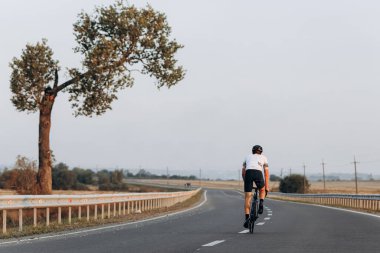 Spor kıyafetleri ve koruyucu kaskla asfalt yolda giden genç bisikletçilerin arka görüntüsü. Aktif ve sağlıklı yaşam tarzı kavramı.