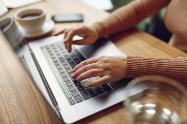 Modern dizüstü bilgisayarın klavyesinde yazan kadın ellerini kapat. Genç bir kadın yerel bir kafede oturuyor ve taşınabilir bilgisayarla internette sörf yapıyor..