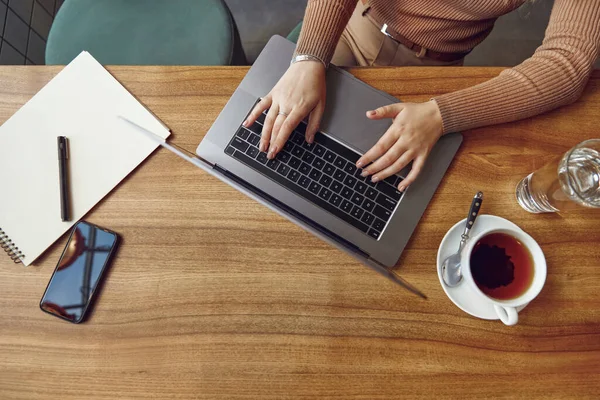 Kafede otururken internetteki kadın serbest sörfçünün kablosuz bilgisayarını kapat. Modern akıllı telefon, defter ve bir fincan sıcak çay. Uzak çalışma kavramı.