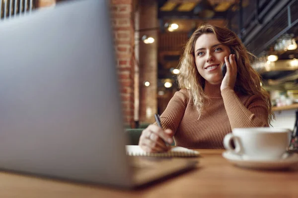 Keyifli Bir Kadın Dizüstü Bilgisayarla Masada Otururken Seyyar Konuşma Yapıyor — Stok fotoğraf
