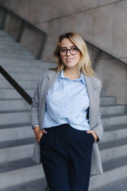 İş kıyafetleri içinde sarı saçlı güzel bir genç kadın ve açık havada poz verirken temiz havanın tadını çıkaran gözler. İnsan kavramı, güven ve çalışma.