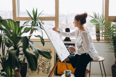 Beyaz gömlekli ve siyah pantolonlu genç bayan ressam sehpaya soyut bir resim çiziyor. Yetenekli kadın sanat stüdyosunda şaheserini yaratıyor..