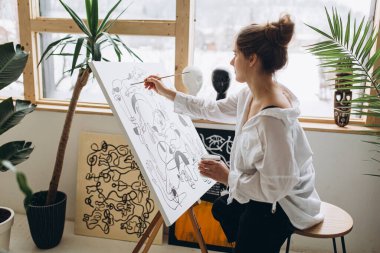 Güzel genç ressam, stüdyoda tuvale siyah beyaz resim çiziyor. Fırça ve yağ renklerini kullanarak günlük kıyafet giyen kadın üstat..