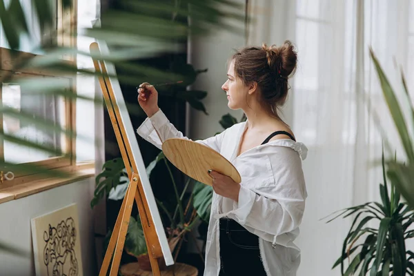 Tuvale fırçayla çizim yapan kadın ressamın yan görüntüsü. Sanat stüdyosunda boş zamanlarında yaratıcı hobilerden hoşlanan genç bir kadın..