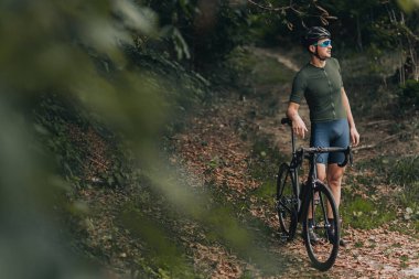 Aktif giyimli beyaz bir adam sabah bisikletinden sonra şehir parkında dinleniyor. Kasklı ve gözlüklü kaslı adam dışarıda siyah bisikletle poz veriyor..