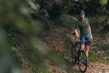 Kasklı beyaz bisikletçi, kasklı ve aynalı gözlüklü. Temiz hava aldıktan sonra siyah bisiklete yaslanıyor. Açık hava aktivitesi ve yaşam tarzı kavramı.