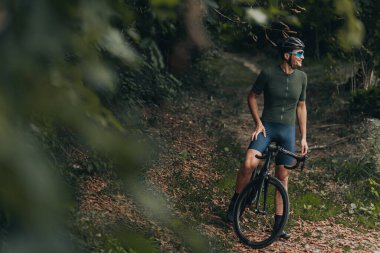 Kasklı ve gözlüklü beyaz bir bisikletçi temiz havada bisikletle dikiliyor, yana bakıyor ve gülümsüyor. İnsan kavramı, spor ve eğlence..