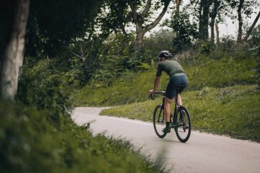 Sabah vakti Green Park 'ta profesyonel bisikletçi eğitiminin arka planında. Spor kıyafetli ve kasklı kasklı adam düzenli olarak temiz havada bisiklet sürüyor..