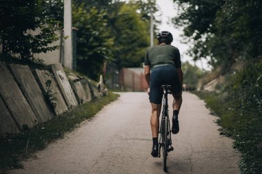 Kaslı adamın sabahları dışarıda bisiklet sürerken arkadan görünüşü. Aktif giyimde profesyonel sporcu ve temiz hava kask eğitimi alıyor..