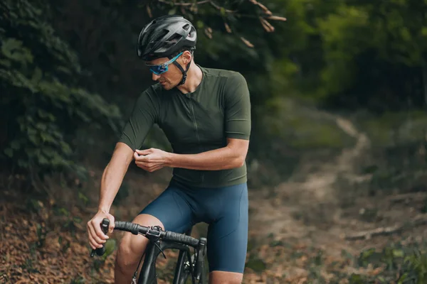 Professional cyclist in sport clothes, safety helmet and glasses preparing for morning cycling at green city park. Concept of active and healthy lifestyles.