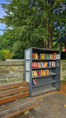 Uberlingen, Almanya - 19 Eylül 2025. Parkta ahşap banklar ve yeşil ağaçlarla dolu açık bir kütüphane. Bilgi ve doğa..