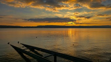 Gölün kıyısında güneşli bir gün batımı. Ön planda yatları indirmek için raylar var.